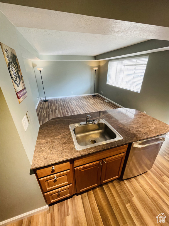 Kitchen featuring a sink, light wood-style flooring, dishwasher, brown cabinets, and dark countertops