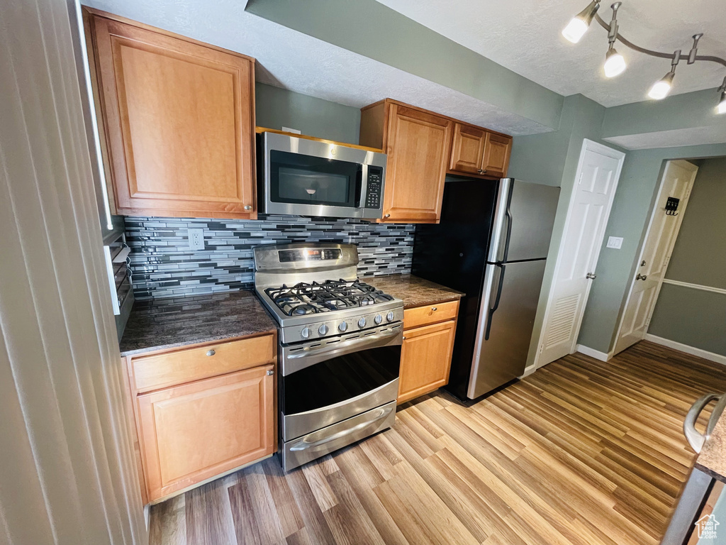 Kitchen featuring appliances with stainless steel finishes, light wood-style flooring, backsplash, and baseboards