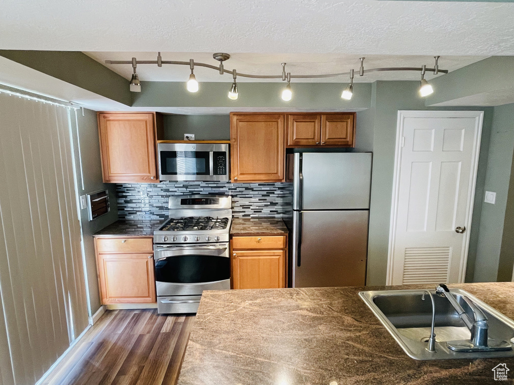 Kitchen with stainless steel appliances, wood finished floors, dark countertops, and tasteful backsplash