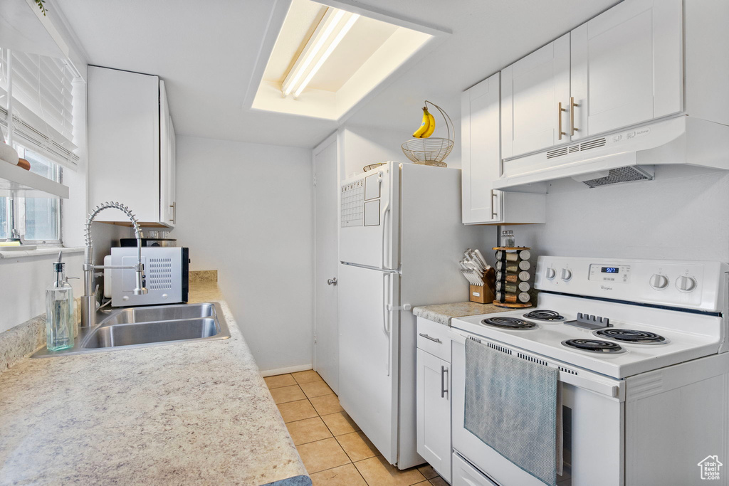 Kitchen featuring white appliances, under cabinet range hood, a sink, white cabinets, and light tile patterned floors