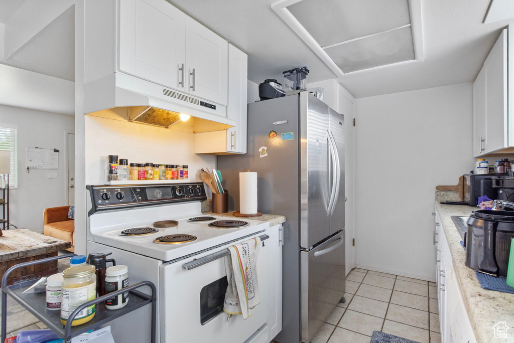 Kitchen featuring white range with electric stovetop, under cabinet range hood, light countertops, white cabinets, and light tile patterned flooring