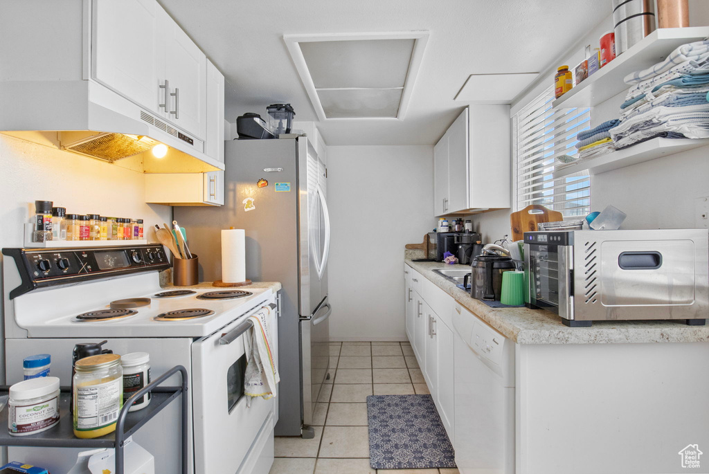 Kitchen featuring white appliances, under cabinet range hood, light countertops, light tile patterned floors, and white cabinets