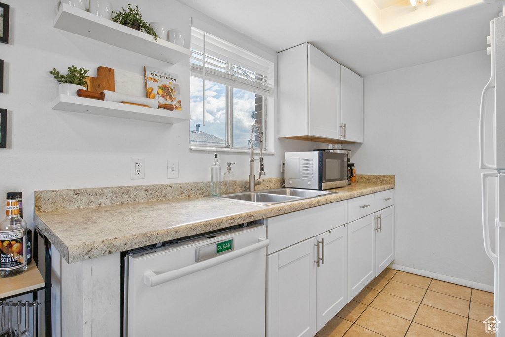 Kitchen with white appliances, a sink, open shelves, light tile patterned floors, and white cabinetry