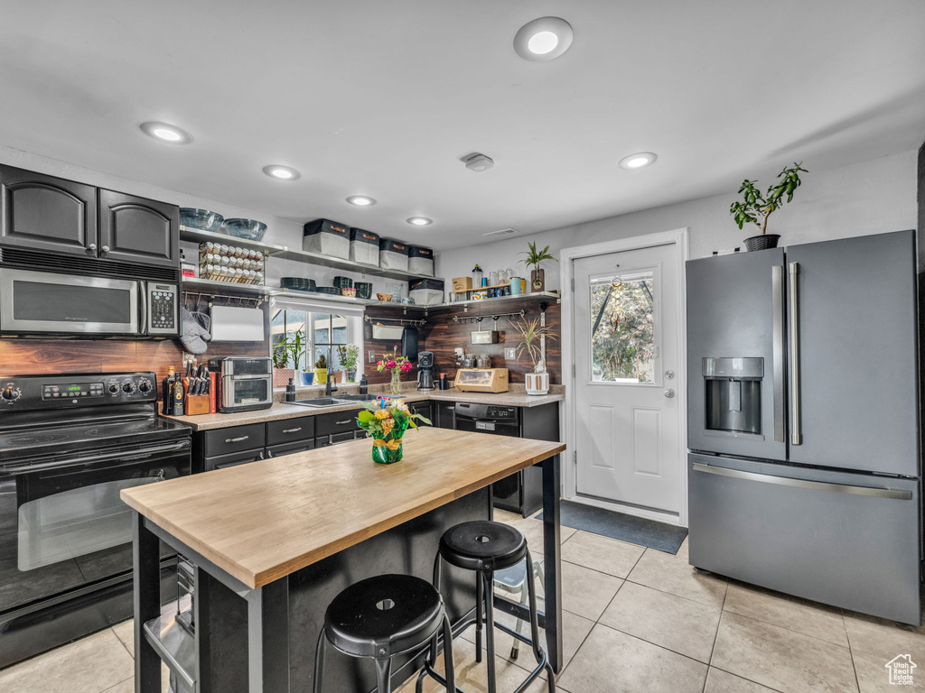 Kitchen with stainless steel appliances, wooden counters, open shelves, light tile patterned floors, and recessed lighting