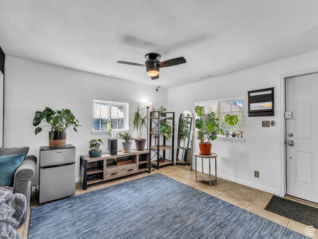 Living area featuring healthy amount of natural light, a ceiling fan, tile patterned flooring, and baseboards