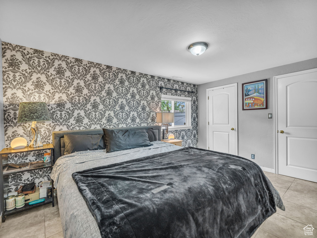 Bedroom featuring wallpapered walls, light tile patterned floors, and baseboards