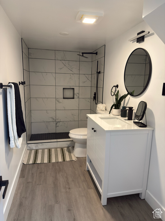Full bath featuring wood finished floors, toilet, vanity, and tiled shower