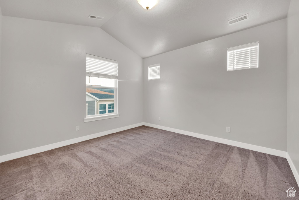 Spare room with vaulted ceiling, carpet floors, and baseboards