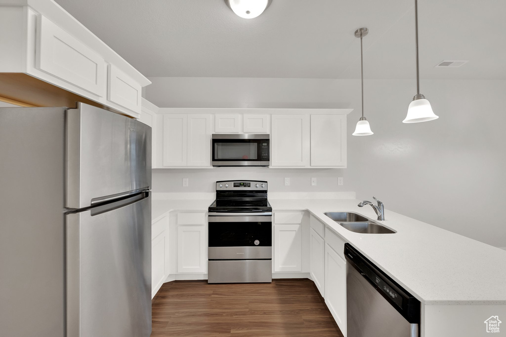 Kitchen with stainless steel appliances, a sink, a peninsula, light countertops, and dark wood-style floors