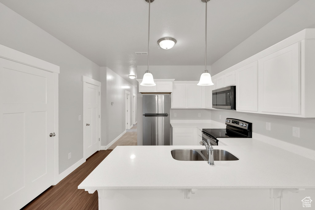 Kitchen featuring appliances with stainless steel finishes, a sink, light countertops, a peninsula, and white cabinets