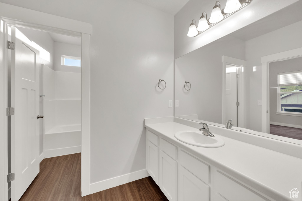 Bathroom with wood finished floors, baseboards, vanity, and washtub / shower combination