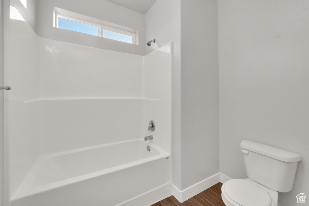Bathroom with baseboards, toilet, wood finished floors, and shower / bathtub combination