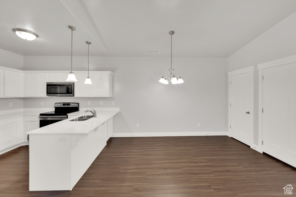 Kitchen with appliances with stainless steel finishes, a sink, a peninsula, white cabinetry, and dark wood-style floors