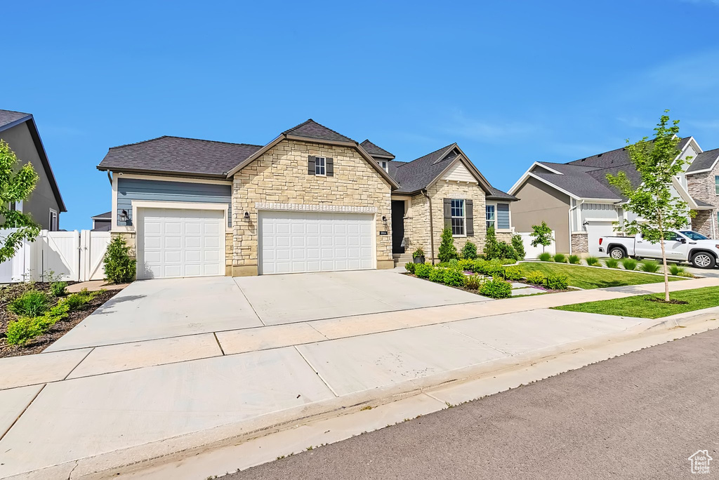 View of front of house with stone siding, an attached garage, concrete driveway, and a shingled roof