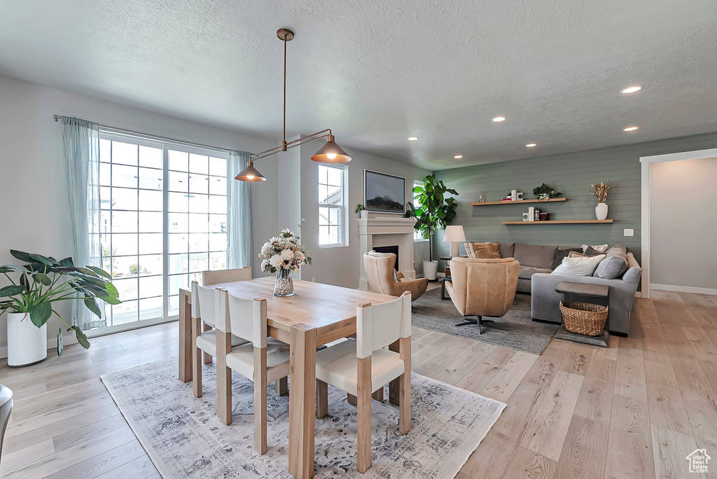 Dining area with a textured ceiling, a fireplace, light wood-type flooring, recessed lighting, and baseboards