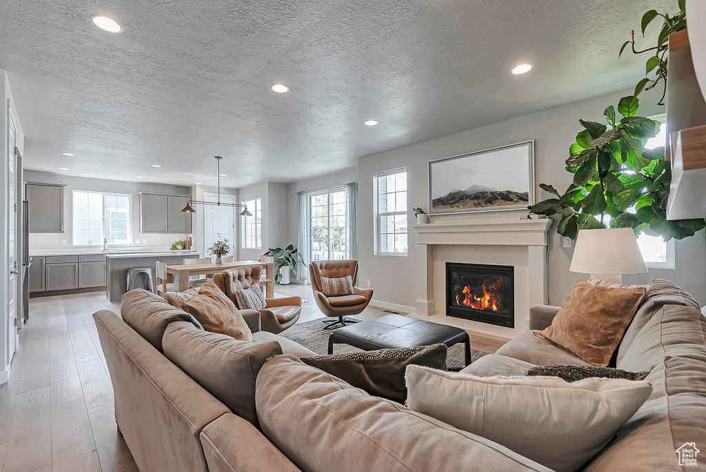 Living area featuring a textured ceiling, a glass covered fireplace, recessed lighting, light wood-style floors, and baseboards