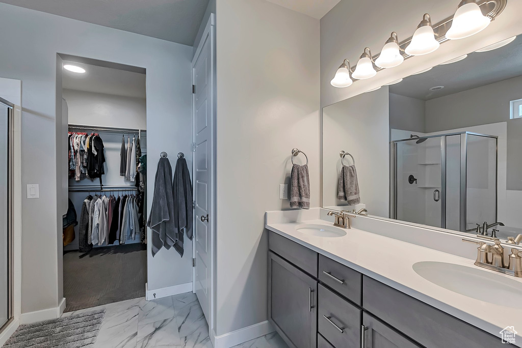 Bathroom with marble look tile flooring, a stall shower, baseboards, double vanity, and a walk in closet