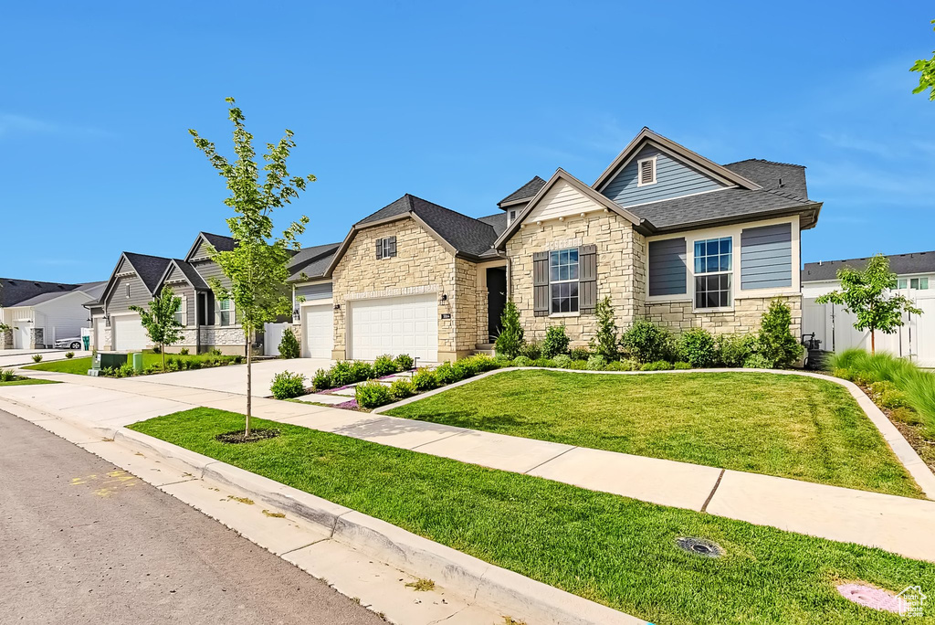 View of front of property with stone siding, a residential view, concrete driveway, and a garage