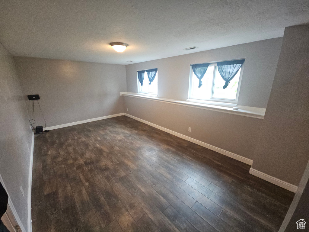 Empty room featuring dark wood-style floors, baseboards, and a textured ceiling
