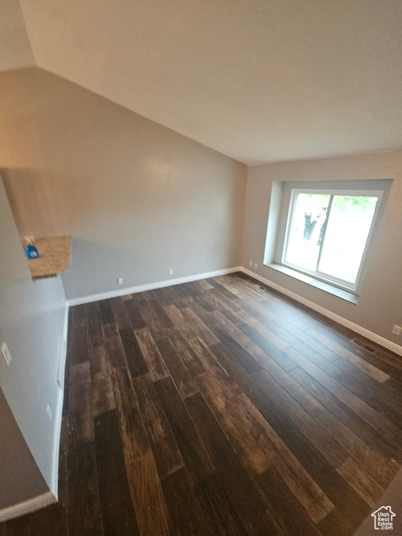 Empty room with dark wood-type flooring, baseboards, and vaulted ceiling