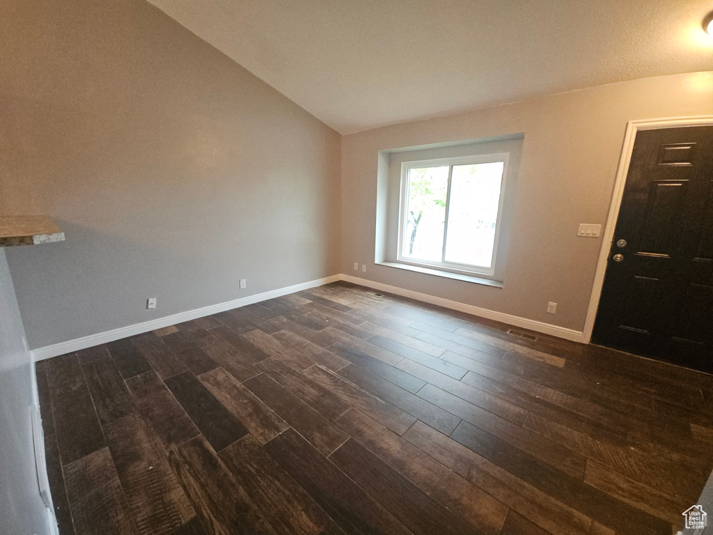 Unfurnished room featuring lofted ceiling, dark wood finished floors, and baseboards