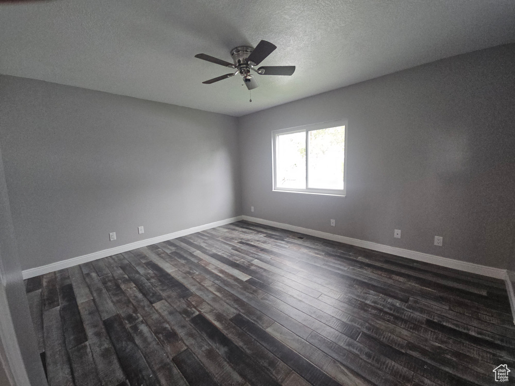 Spare room with dark wood-type flooring, ceiling fan, baseboards, and a textured ceiling