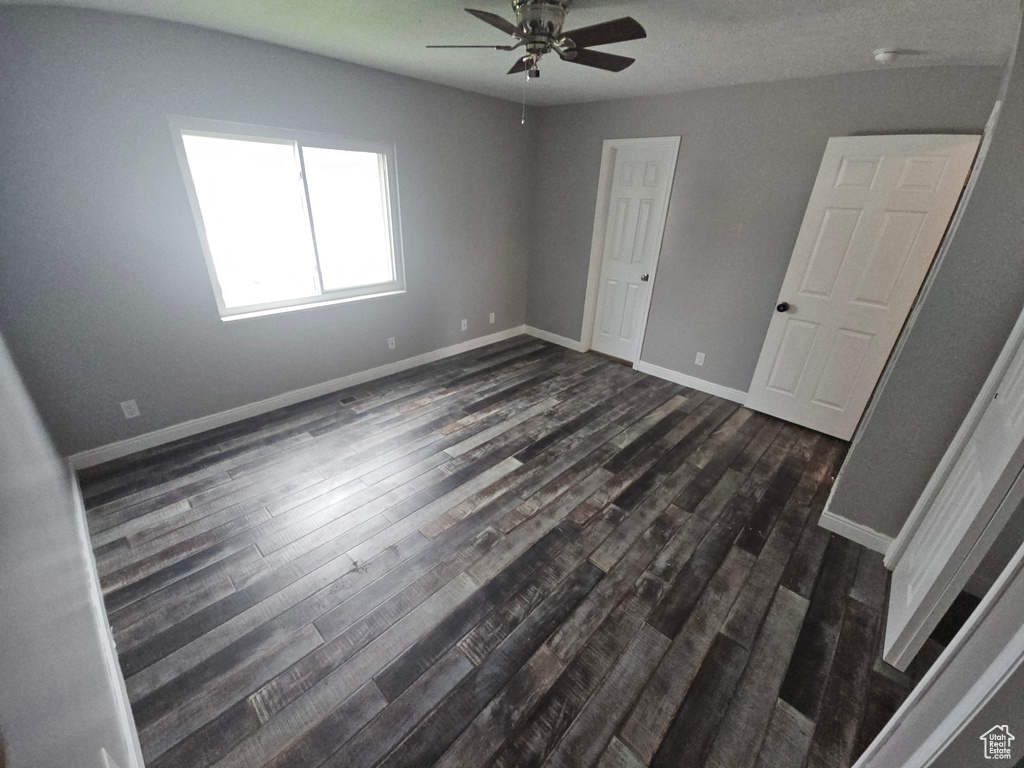 Unfurnished bedroom with dark wood-style floors, baseboards, and a ceiling fan