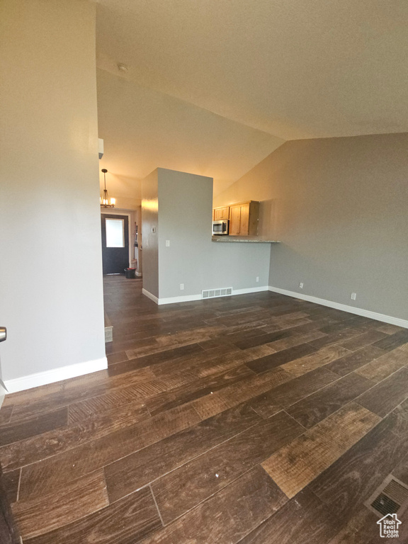 Unfurnished living room with dark wood-style floors, vaulted ceiling, and baseboards