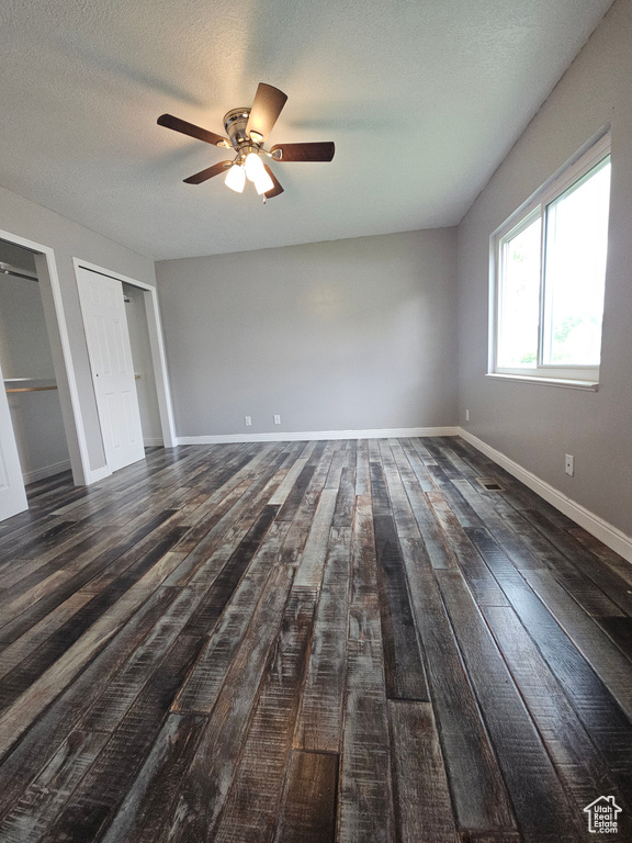 Unfurnished bedroom with wood finished floors, two closets, baseboards, ceiling fan, and a textured ceiling