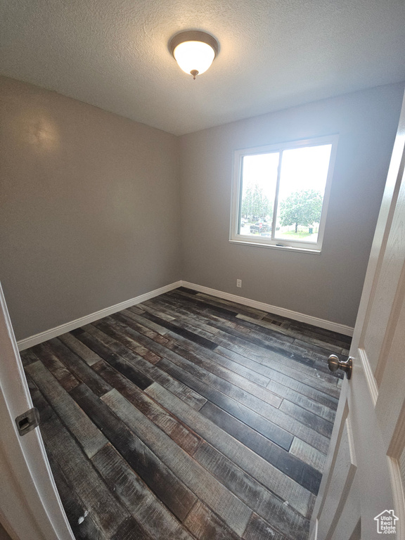 Unfurnished room with dark wood-style flooring, a textured ceiling, and baseboards