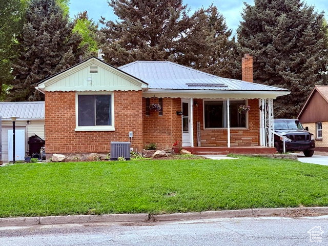 View of front facade featuring covered porch, a front yard, brick siding, and a chimney