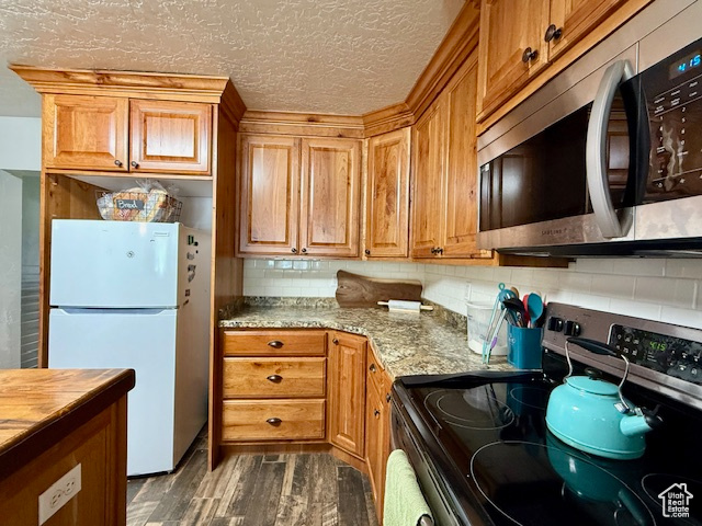 Kitchen with appliances with stainless steel finishes, dark wood finished floors, tasteful backsplash, brown cabinetry, and a textured ceiling