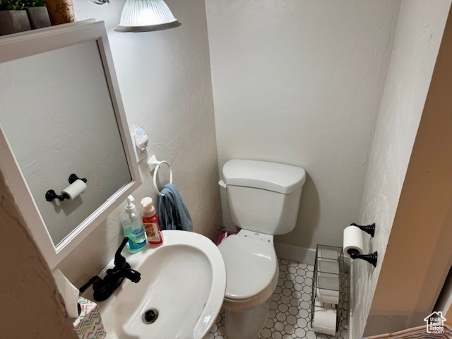 Half bathroom featuring a sink, toilet, tile patterned floors, and a textured wall