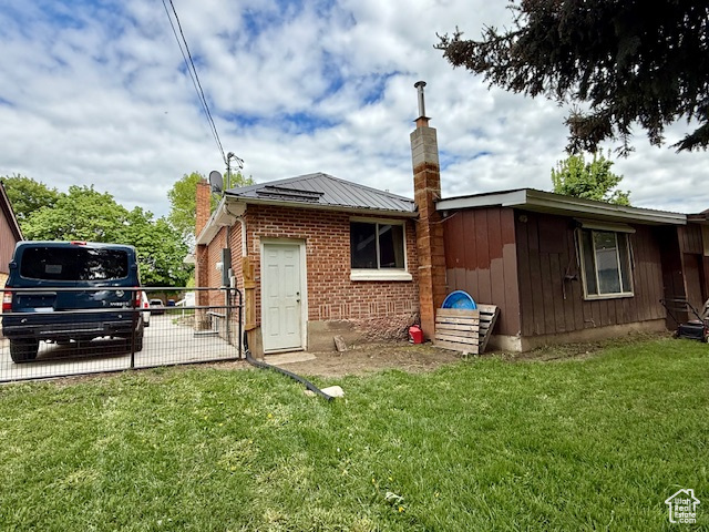 Back of house with a chimney, brick siding, and metal roof