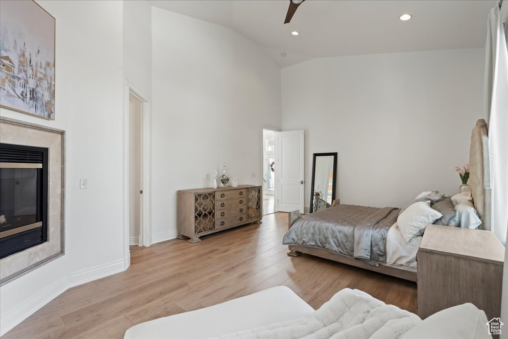 Bedroom featuring a glass covered fireplace, wood finished floors, baseboards, high vaulted ceiling, and recessed lighting