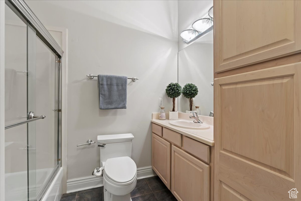 Full bathroom featuring toilet, vanity, baseboards, tile patterned flooring, and shower / bath combination with glass door