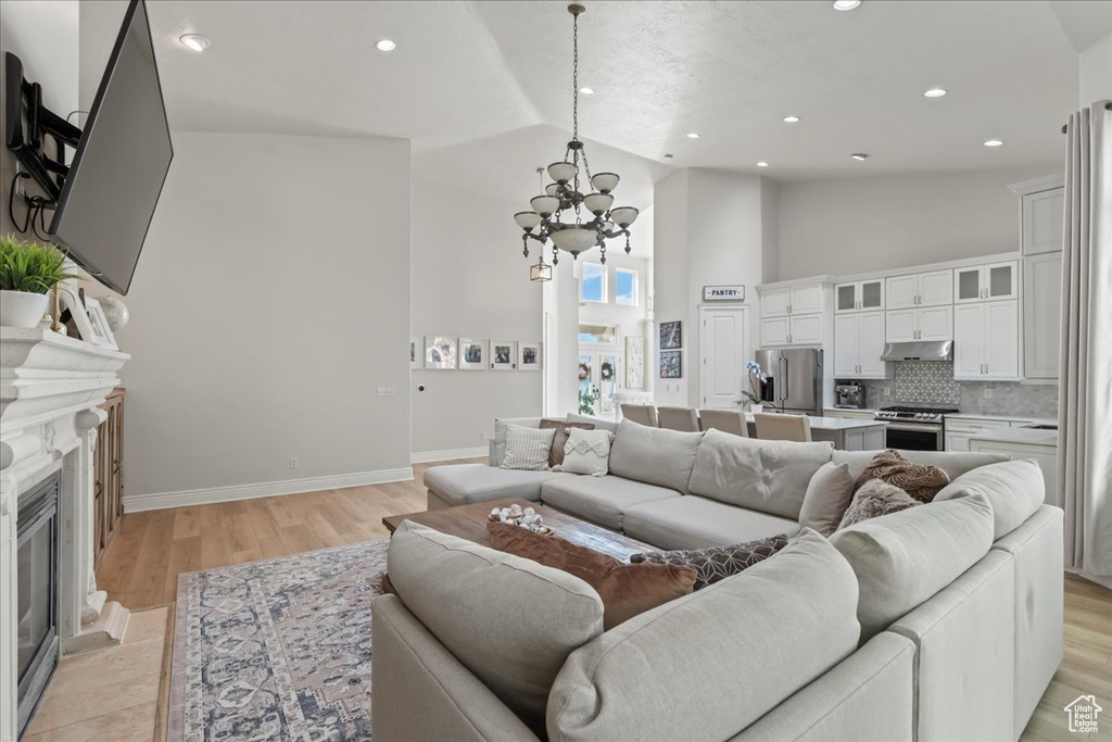Living area with a chandelier, a fireplace with flush hearth, baseboards, high vaulted ceiling, and light wood-style floors