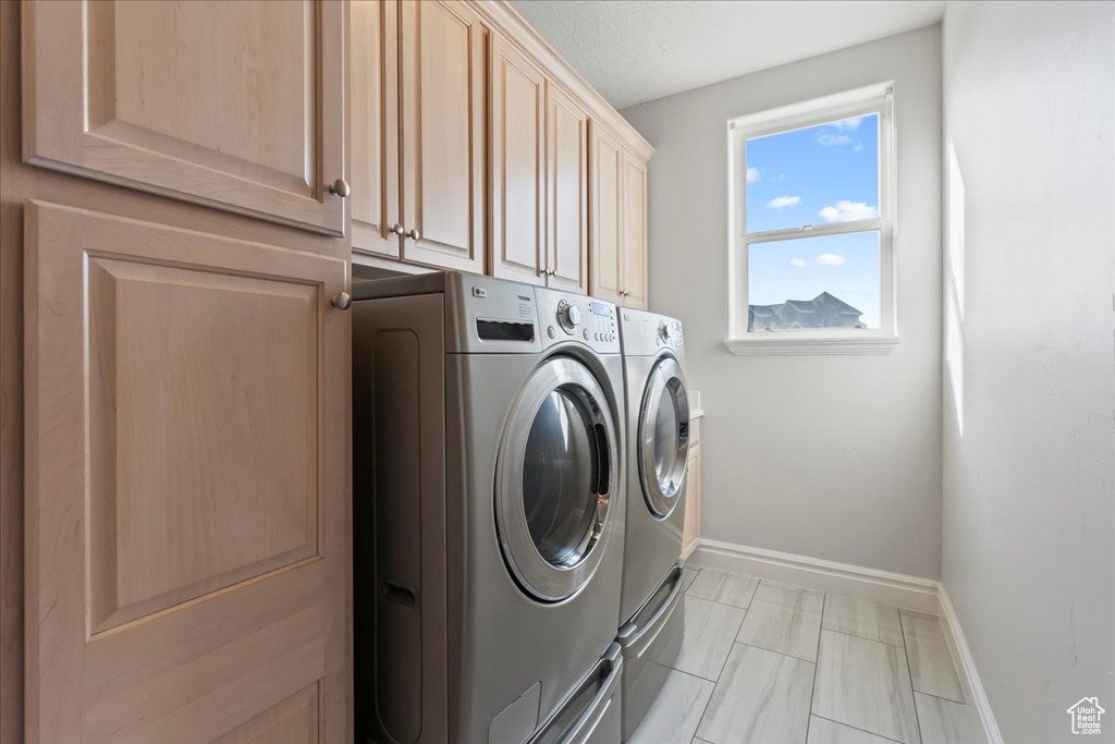 Laundry room featuring washing machine and clothes dryer, cabinet space, and baseboards