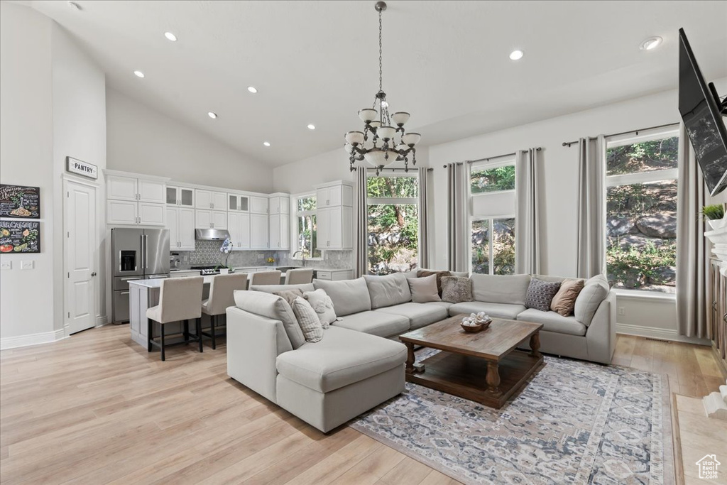 Living room with a chandelier, recessed lighting, light wood-style floors, high vaulted ceiling, and baseboards