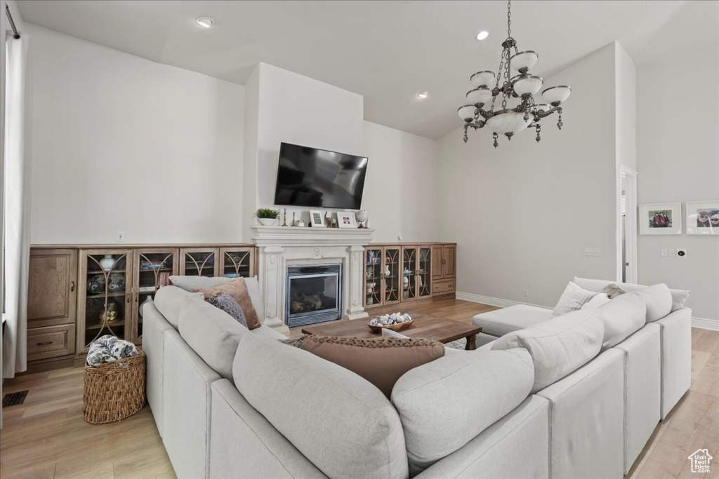 Living room featuring lofted ceiling, light wood-style floors, a glass covered fireplace, a chandelier, and recessed lighting