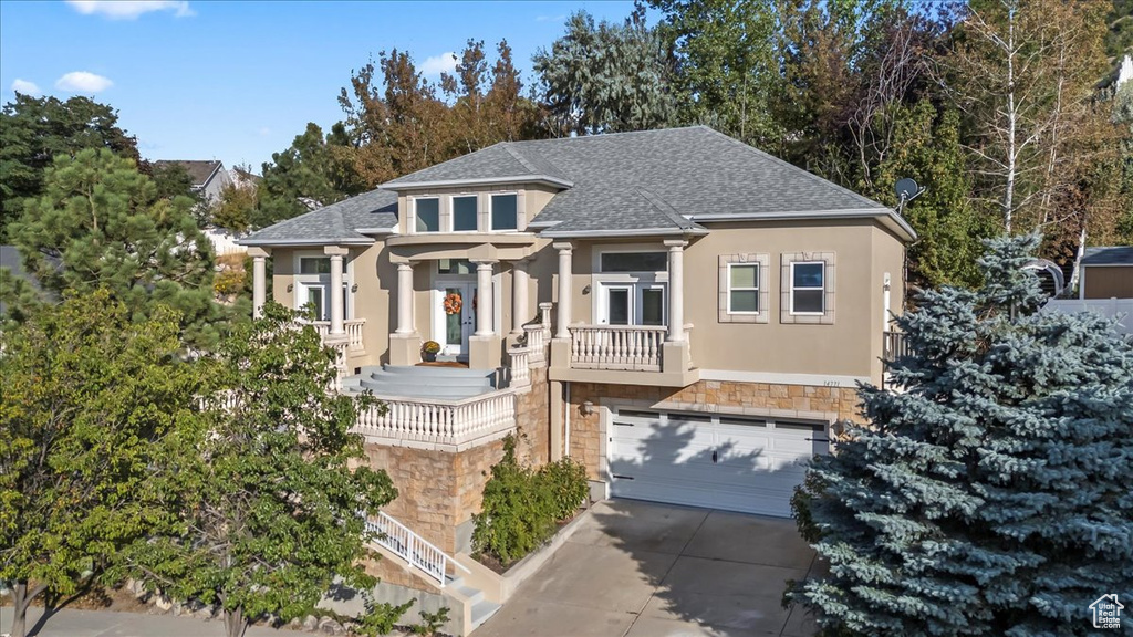 View of front facade featuring a shingled roof, stone siding, concrete driveway, stucco siding, and an attached garage