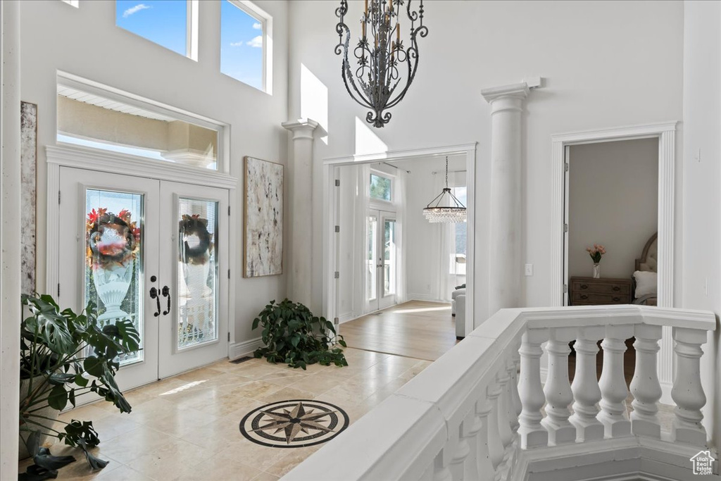 Foyer with french doors, a chandelier, plenty of natural light, a high ceiling, and decorative columns