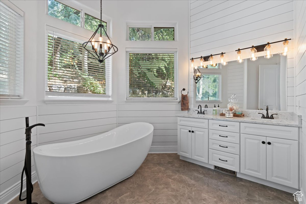 Bathroom featuring a chandelier, wooden walls, double vanity, a freestanding tub, and a high ceiling