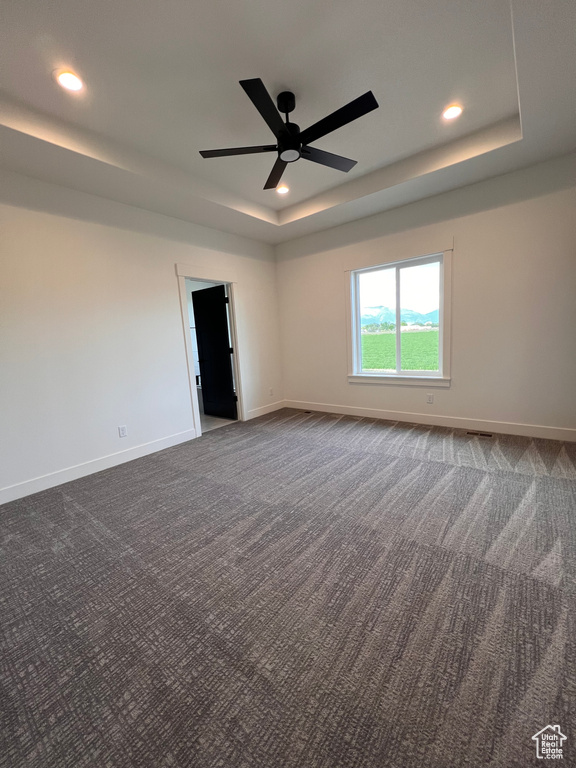 Unfurnished room featuring a tray ceiling, dark colored carpet, baseboards, and recessed lighting