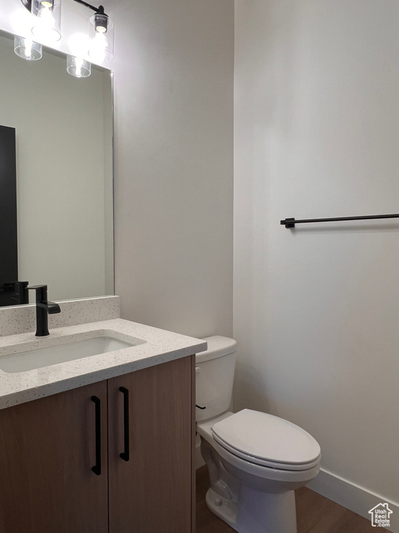 Half bath with toilet, vanity, baseboards, and wood finished floors