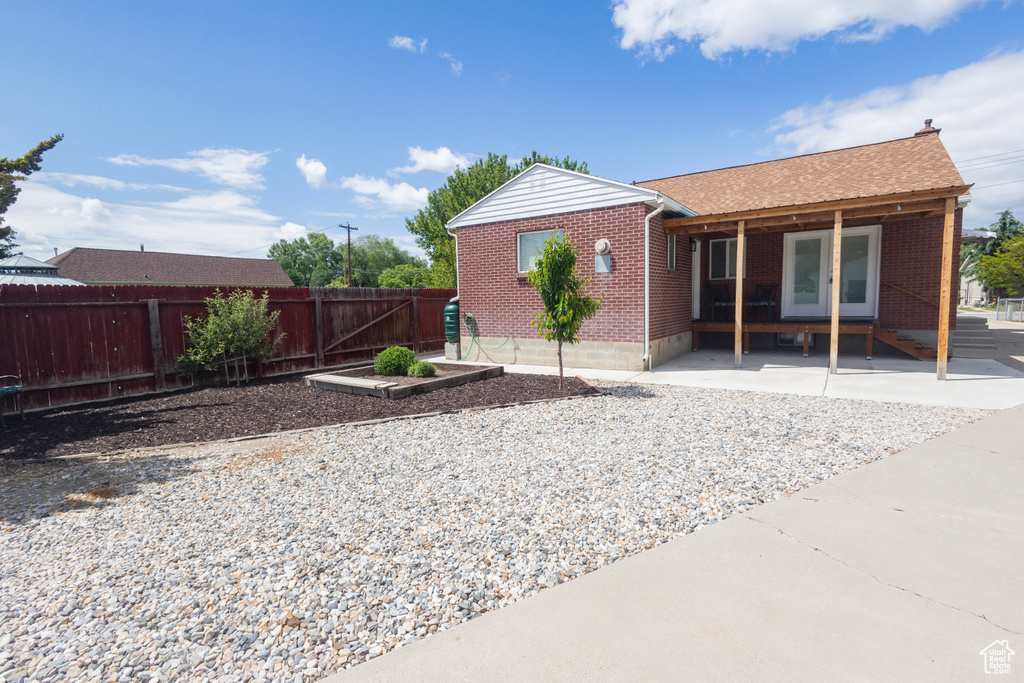 Back of house with brick siding, a garden, a shingled roof, and a patio area