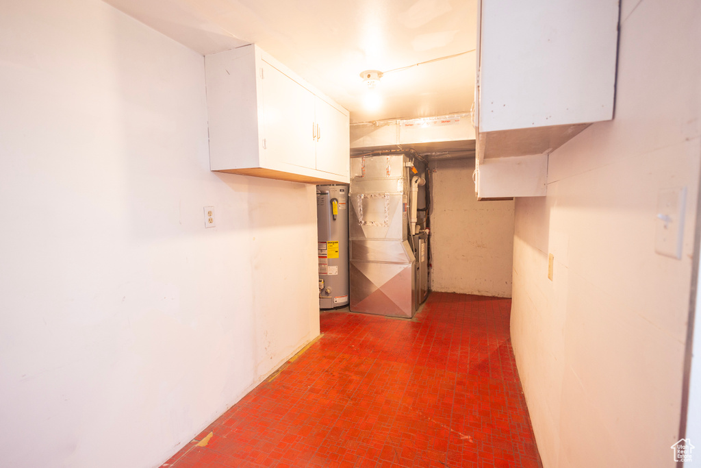 Unfinished below grade area featuring brick patterned flooring, water heater, and heating unit