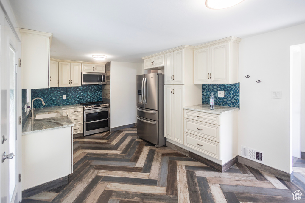 Kitchen featuring appliances with stainless steel finishes, cream cabinets, a sink, and decorative backsplash