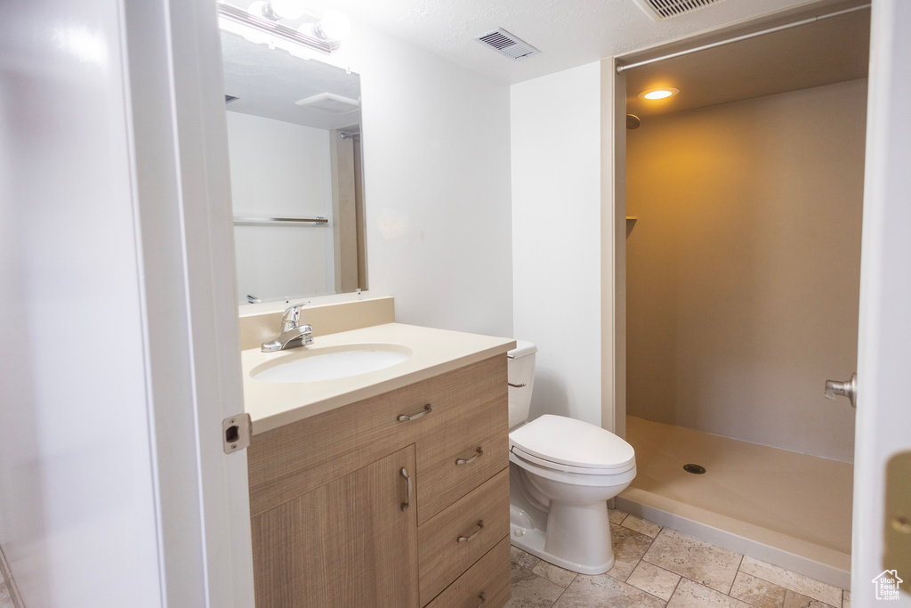 Full bathroom with toilet, a shower stall, vanity, and stone tile floors