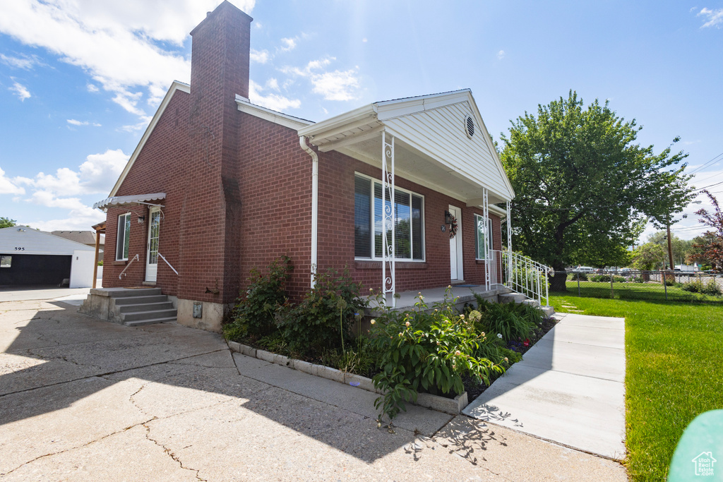 View of home\'s exterior featuring a porch, brick siding, a chimney, an outbuilding, and a yard